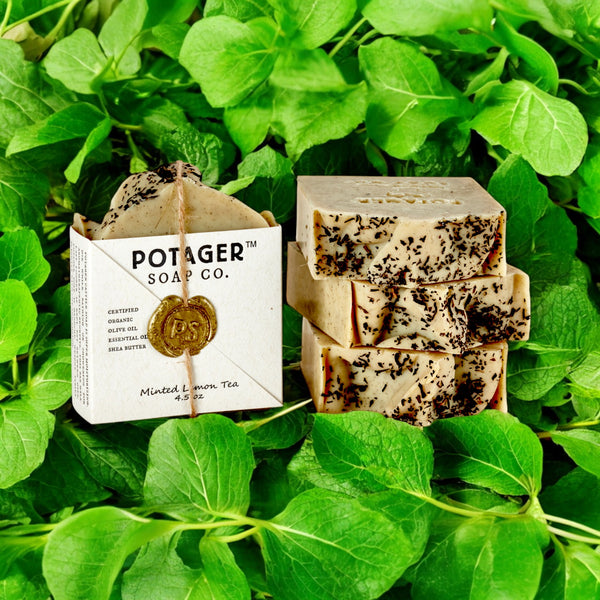 A bar of Mint Lemon Tea soap placed on a bed of fresh mint leaves, with the product packaging visible in the background.