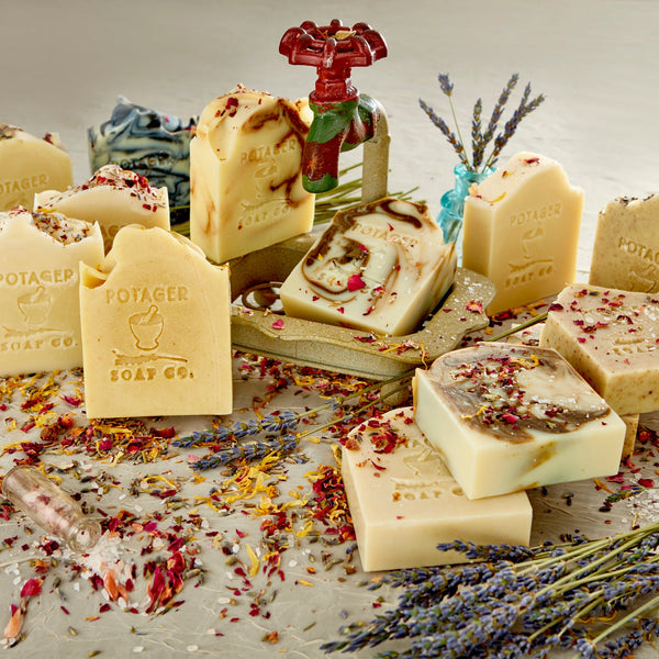 An assortment of Potager natural soap bars with slight visual imperfections, displayed on a surface with scattered dried flowers and botanicals.