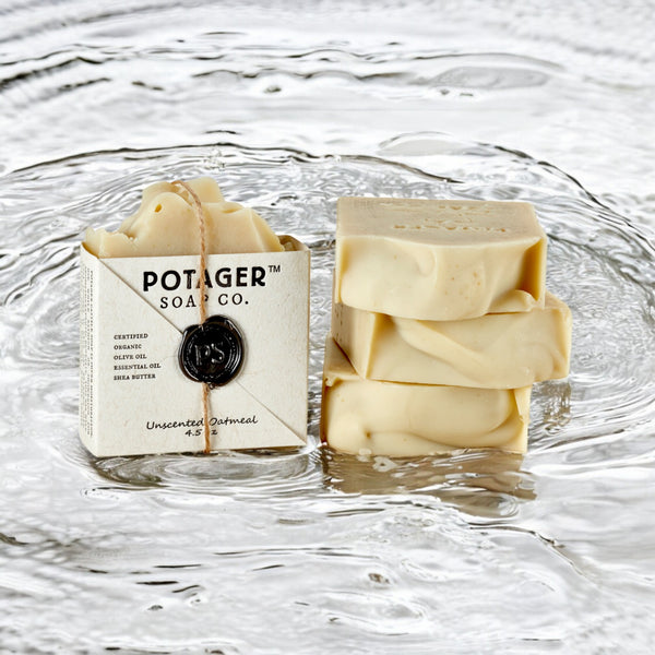 Three bars of Potager’s Unscented Oatmeal Soap floating on water, with the soap packaging visible in the background.