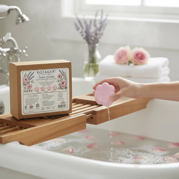 Potager Soap Co. Secret Garden flower-shaped pink bath bomb being held over a bathtub with rose petals in the water.